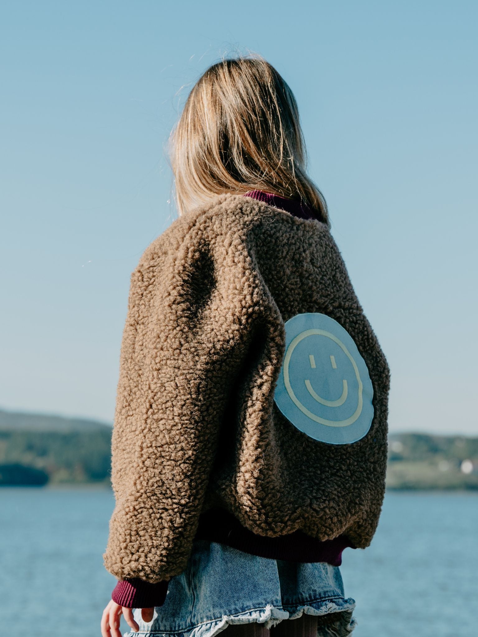 [Modelka ma 133 cm wzrostu i nosi kurtkę w rozmiarze 9-10 lat] kurtka dziecięca bomberka wełniana merino teddy brown stylizacja outfit tył dziecko uśmiech